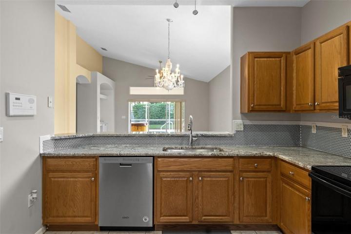 Solid wood cabinets with granite countertops. Looking from kitchen, across breakfast bar into dining area, great room, then beyond out to the lanai and pool.