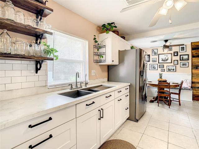 kitchen has been tastefully updated with white shaker-style cabinets, stainless-steel appliances, quartz countertops, modern open shelving, and subway tile backsplash. The kitchen extends to an eat-in breakfast nook furnished with a long built-in bench that maximizes space and seating while providing storage space underneath
