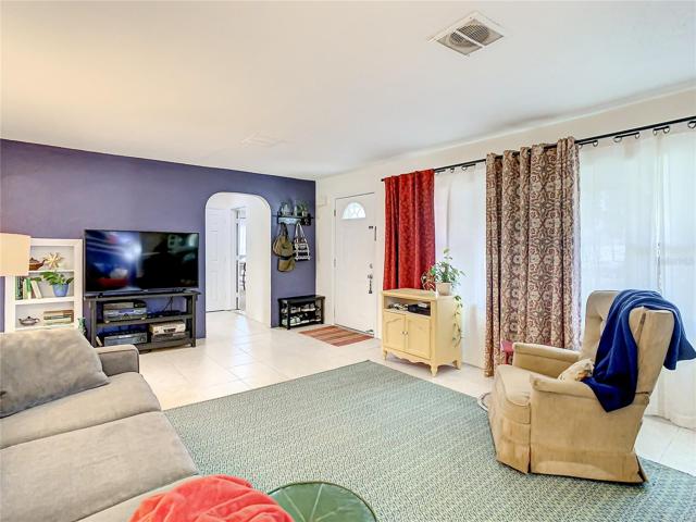 the formal living room that features large windows and easy maintenance tile flooring that flows through to the family room, hallway to the bedrooms, and into the kitchen