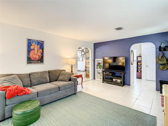 the formal living room that features large windows and easy maintenance tile flooring that flows through to the family room, hallway to the bedrooms, and into the kitchen