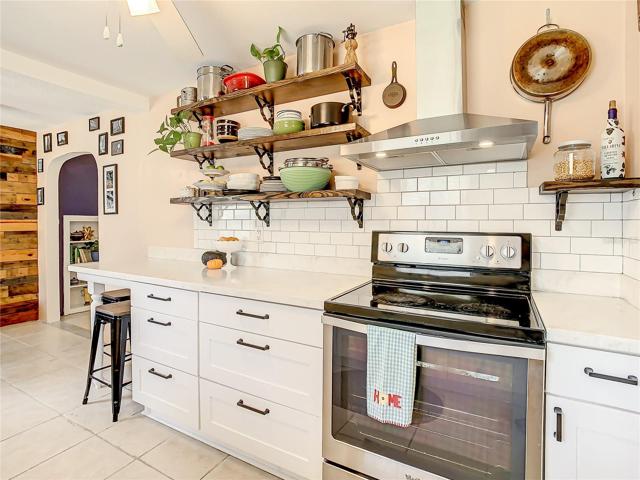 kitchen has been tastefully updated with white shaker-style cabinets, stainless-steel appliances, quartz countertops, modern open shelving, and subway tile backsplash. The kitchen extends to an eat-in breakfast nook furnished with a long built-in bench that maximizes space and seating while providing storage space underneath