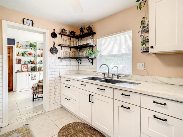 kitchen has been tastefully updated with white shaker-style cabinets, stainless-steel appliances, quartz countertops, modern open shelving, and subway tile backsplash. The kitchen extends to an eat-in breakfast nook furnished with a long built-in bench that maximizes space and seating while providing storage space underneath