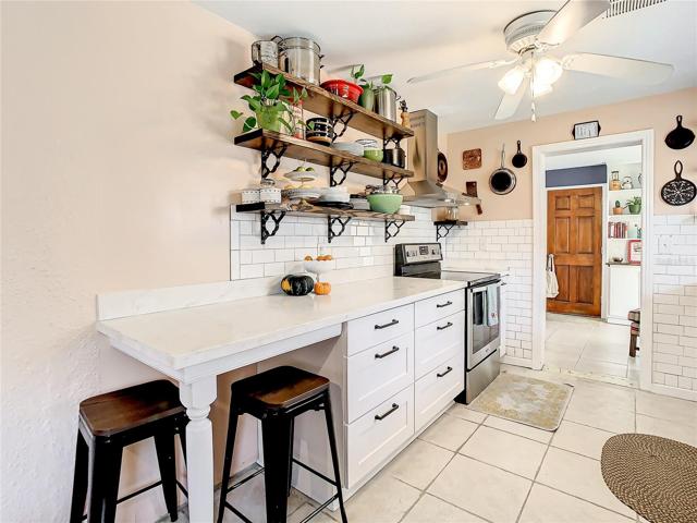 kitchen has been tastefully updated with white shaker-style cabinets, stainless-steel appliances, quartz countertops, modern open shelving, and subway tile backsplash. The kitchen extends to an eat-in breakfast nook furnished with a long built-in bench that maximizes space and seating while providing storage space underneath