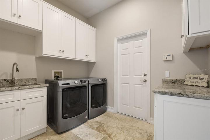 Tons of storage in this fully equipped laundry room with extra cabinetry, convenient sink and ample stone counters for folding area.