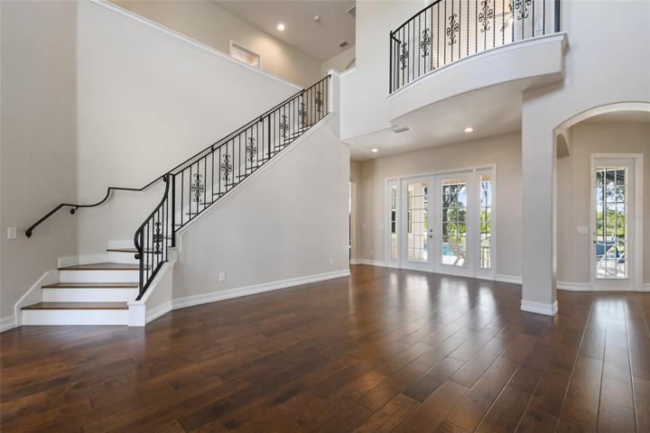 Dramatic view of the living room and grand staircase adorned with real wrought iron railing upon entering the front door you are greeted with views of the outdoor living space, screened pool and water view.behind the french doors