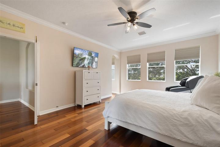 The natural light floods the master bedroom and showcases the crown molding, window treatments, wood flooring, new ceiling fan and neutral wall color.
