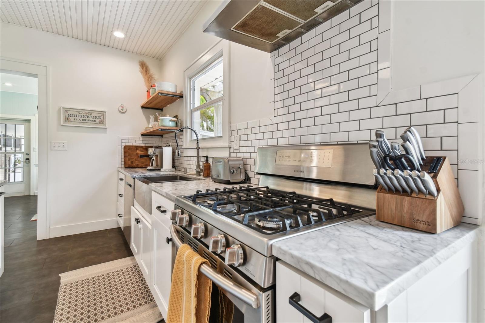 Stainless gas stove with matching stainless chimney-style range hood. Vintage subway tile.