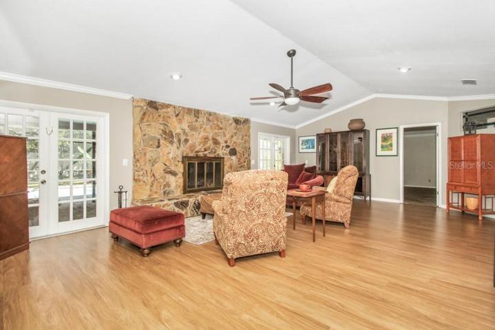 As you continue inside the home, you will notice one of the many standout features of this home is the spacious living room with cathedral ceilings, wood-burning fireplace, and two sets of French doors that lead out to the large, screened pool area.