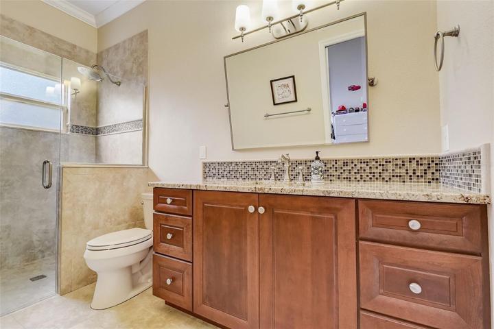 Bathroom with granite counters, tile backsplash & tiled shower with frameless glass door