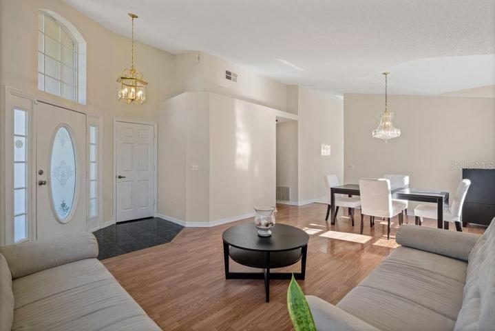 Foyer leading to living room and dining area. A coat closet conveniently located by the front door entrance for those rainy or cool days in Florida, or for extra storage. Great natural light provided by the window designs and the vaulted ceilings!