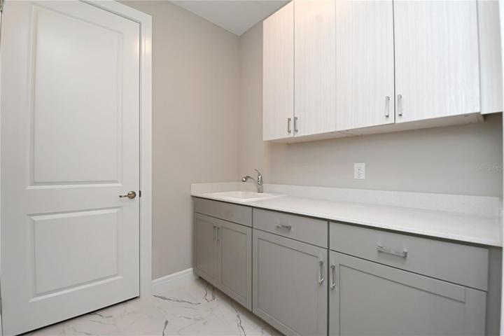 The laundry room features high-end cabinetry with stone countertops, a sink and closet for storage.
