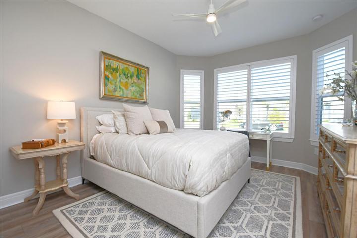 Bedroom 3 boasts a bay window illuminating a custom-built closet and luxury vinyl flooring. Comfort meets style with a ceiling fan, plantation shutters, and tranquil hues