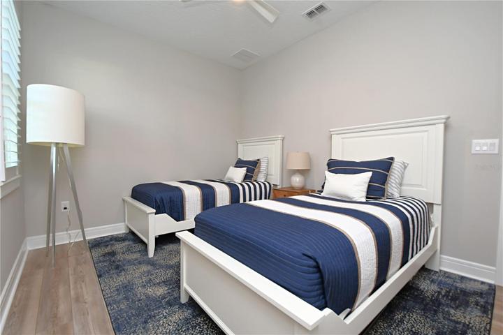 Bedroom three is appointed with a bespoke built-in closet, high-end vinyl plank flooring, a breezy ceiling fan, plantation shutters, and a soothing, neutral color scheme.