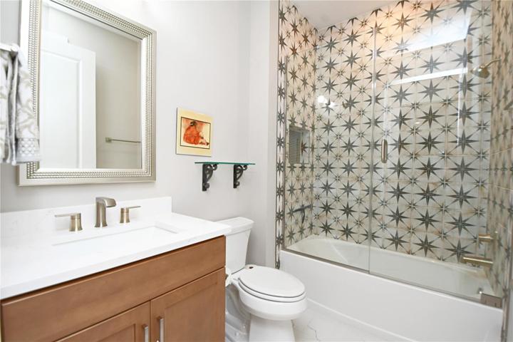 Bathroom 2 enchants with a mirrored vanity offering ample storage beneath modern lighting. The seamless glass-enclosed tub with a sublime tile backdrop promises relaxation.