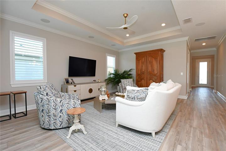 The great room features a tray ceiling, a chic ceiling fan, plantation shutters, crown molding and luxury vinyl flooring.