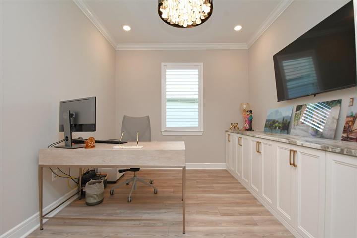 The flex room, a versatile space encased in French doors, serves as a home office. It's a testament to modern design, featuring recessed lighting, luxury vinyl flooring, plantation shutters, and a built-in wall-to-wall cabinet.