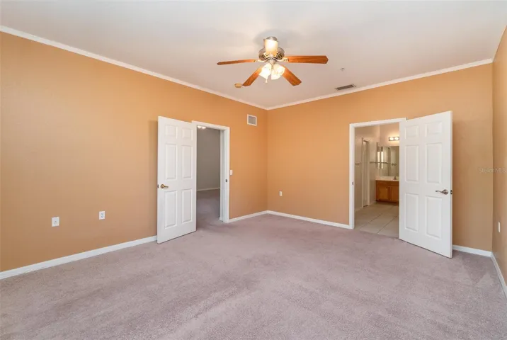 Primary bedroom boasting high ceilings, fan, an en-suite bathroom, and a walk-in closet.