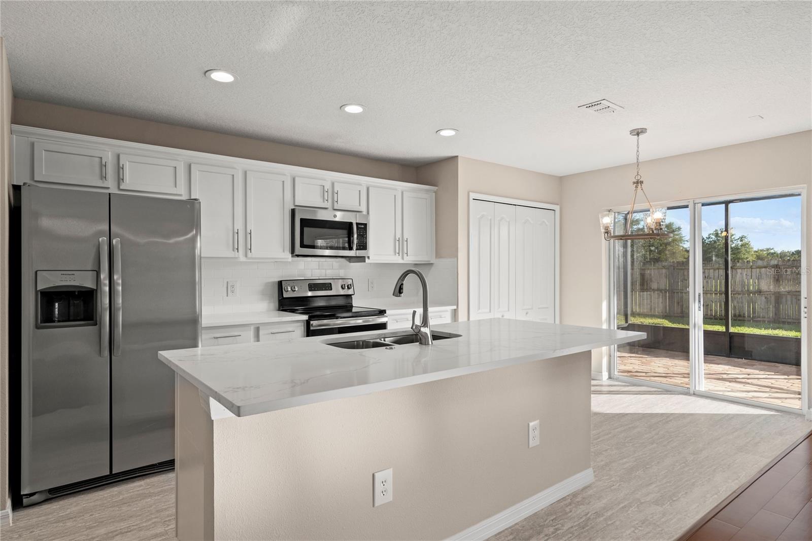 Open kitchen boasts quartz countertops, a contemporary white subway tile backsplash, luxury vinyl plank flooring, and stainless steel appliances. The expansive center island, complete with a breakfast bar, adjoins the family room adorned with wood flooring.