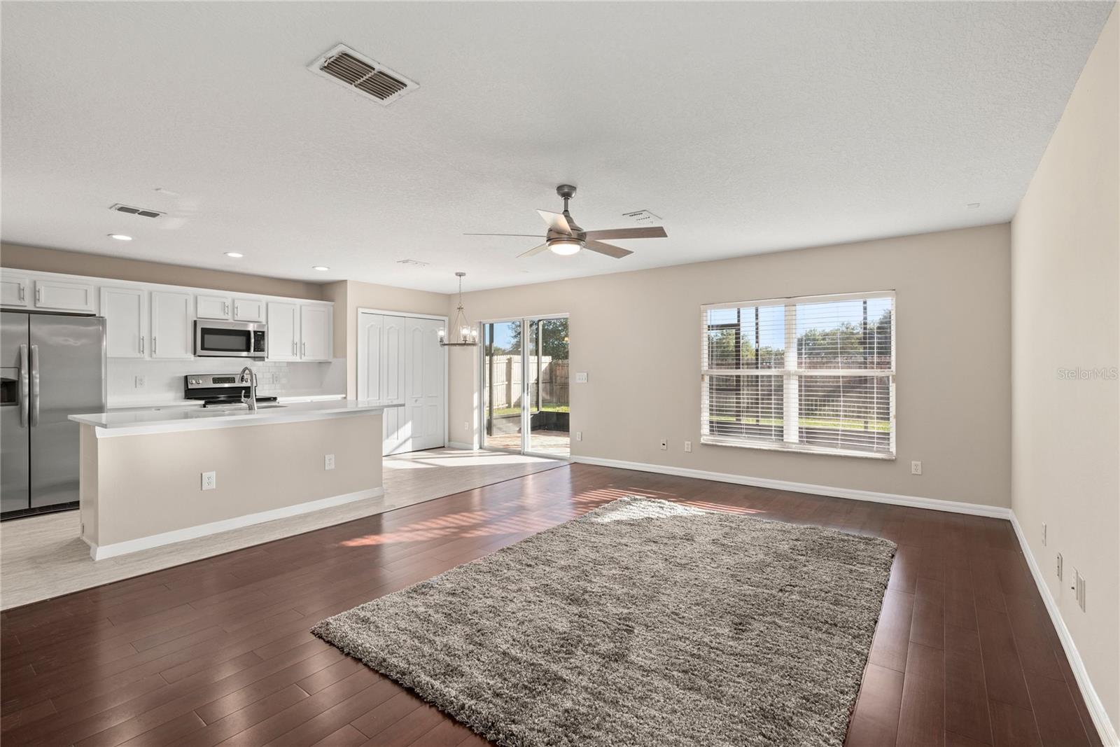 Open kitchen boasts quartz countertops, a contemporary white subway tile backsplash, luxury vinyl plank flooring, and stainless steel appliances. The expansive center island, complete with a breakfast bar, adjoins the family room adorned with wood flooring.
