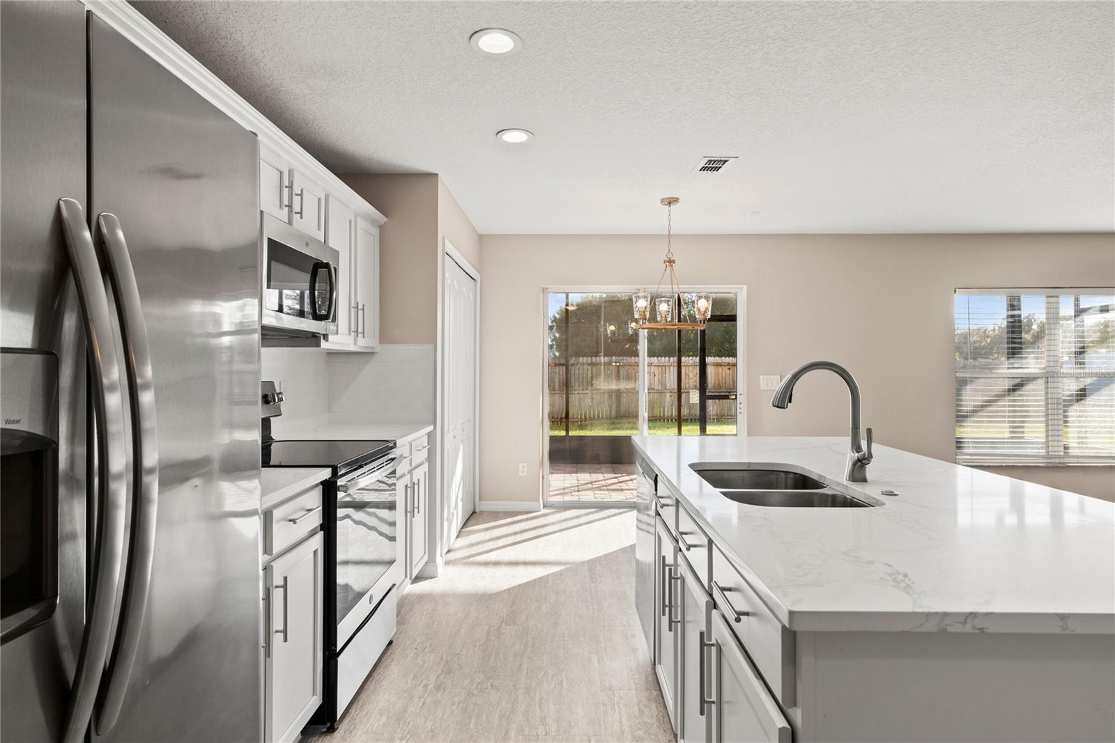 Open kitchen boasts quartz countertops, a contemporary white subway tile backsplash, luxury vinyl plank flooring, and stainless steel appliances. The expansive center island, complete with a breakfast bar, adjoins the family room adorned with wood flooring.