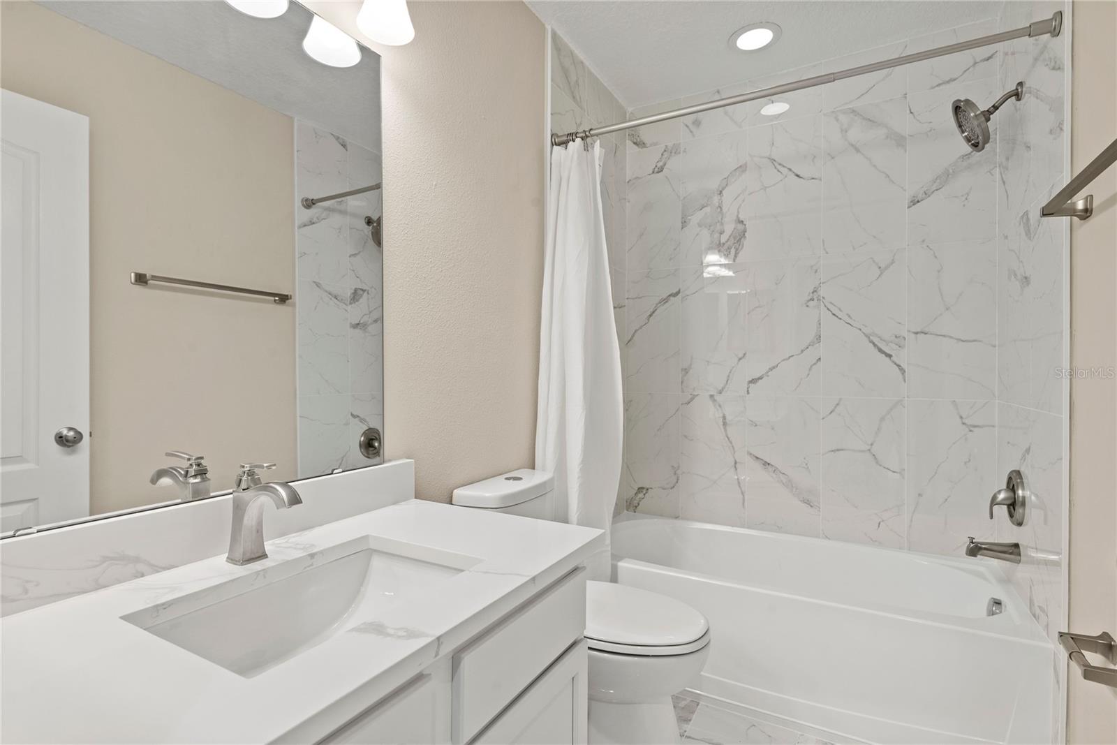 Newly designed second level hallway bath with quartz vanity, marble tile flooring and tiled shower/tub combo