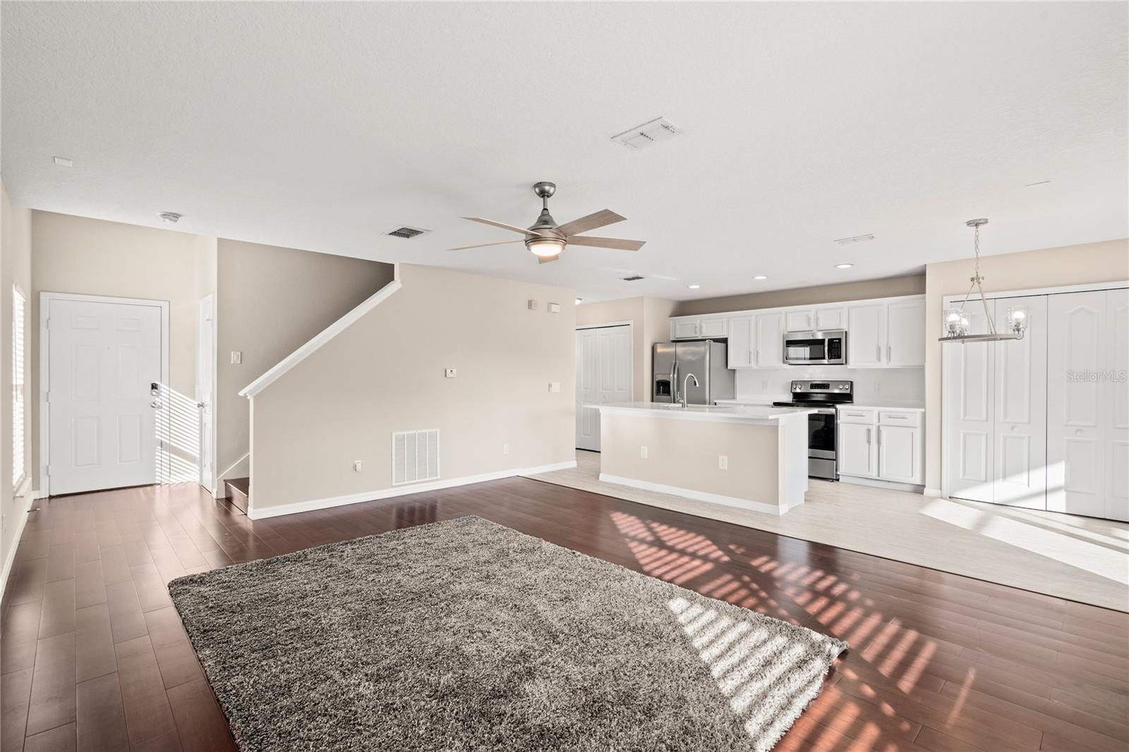 Open kitchen boasts quartz countertops, a contemporary white subway tile backsplash, luxury vinyl plank flooring, and stainless steel appliances. The expansive center island, complete with a breakfast bar, adjoins the family room adorned with wood flooring.