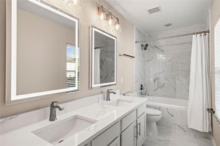 Newly redesigned master bath exudes sophistication, featuring a double quartz top vanity with LED dimmable anti-fog mirrors, marble tile flooring, and a generously-sized shower/tub combination