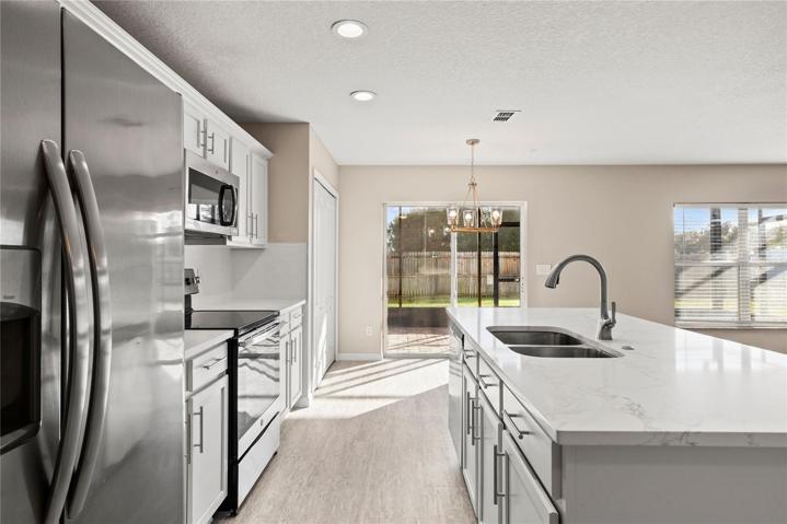 Open kitchen boasts quartz countertops, a contemporary white subway tile backsplash, luxury vinyl plank flooring, and stainless steel appliances. The expansive center island, complete with a breakfast bar, adjoins the family room adorned with wood flooring.