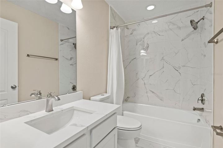Newly designed second level hallway bath with quartz vanity, marble tile flooring and tiled shower/tub combo