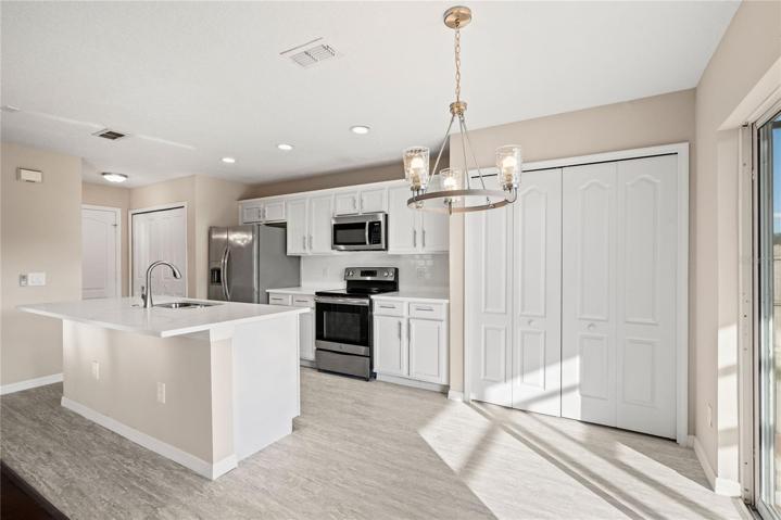 Open kitchen boasts quartz countertops, a contemporary white subway tile backsplash, luxury vinyl plank flooring, and stainless steel appliances. The expansive center island, complete with a breakfast bar, adjoins the family room adorned with wood flooring.