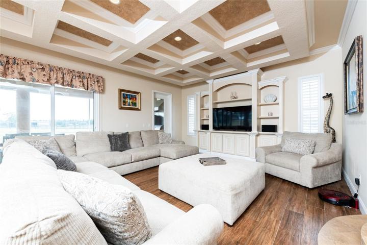 Family Room Showcasing Coffered Ceiling, Built In Entertainment Center, and Triple Sliding Glass Doors that Fully Open to the Pool and Summer Kitchen
