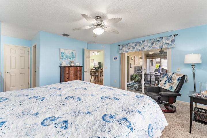View from back corner of PRIMARY BEDROOM - Door on L leads to WALK-IN Shower, Adjacent open doorway (L) leads to WALK-IN CLOSET, Entrance to PRIMARY BR (open door center), SLIDING GLASS DOORS leading to SCREEN ENCLOSED LANAI in rear of home.