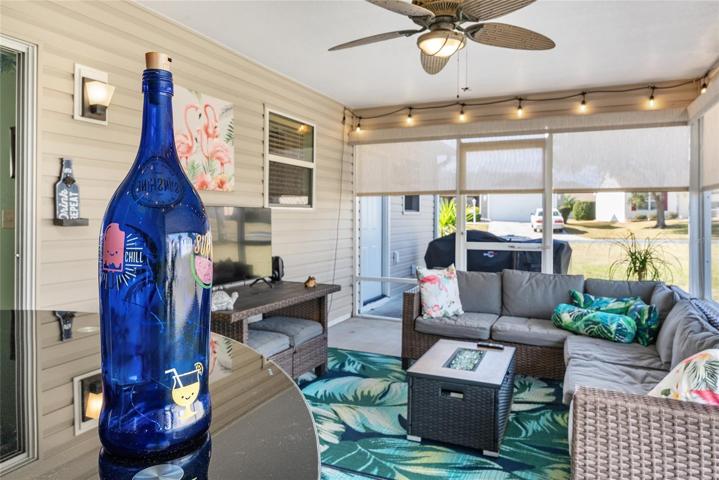 View of SCREEN ENCLOSED LANAI looking over DRY BAR CONSOLE. Note: GAS BURNING FIREPIT in front of sectional couch, SOLAR SHADES surrounding the perimeter of lanai, and festive lights for outdoor gatherings.