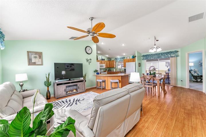 View from FOYER - LIVING ROOM (front L), DINING ROOM (back R), doorway to Primary Bedroom (back R) & Kitchen (L center back). SLIDING GLASS DOORS lead to SCREEN ENCLOSED LANAI (center back).