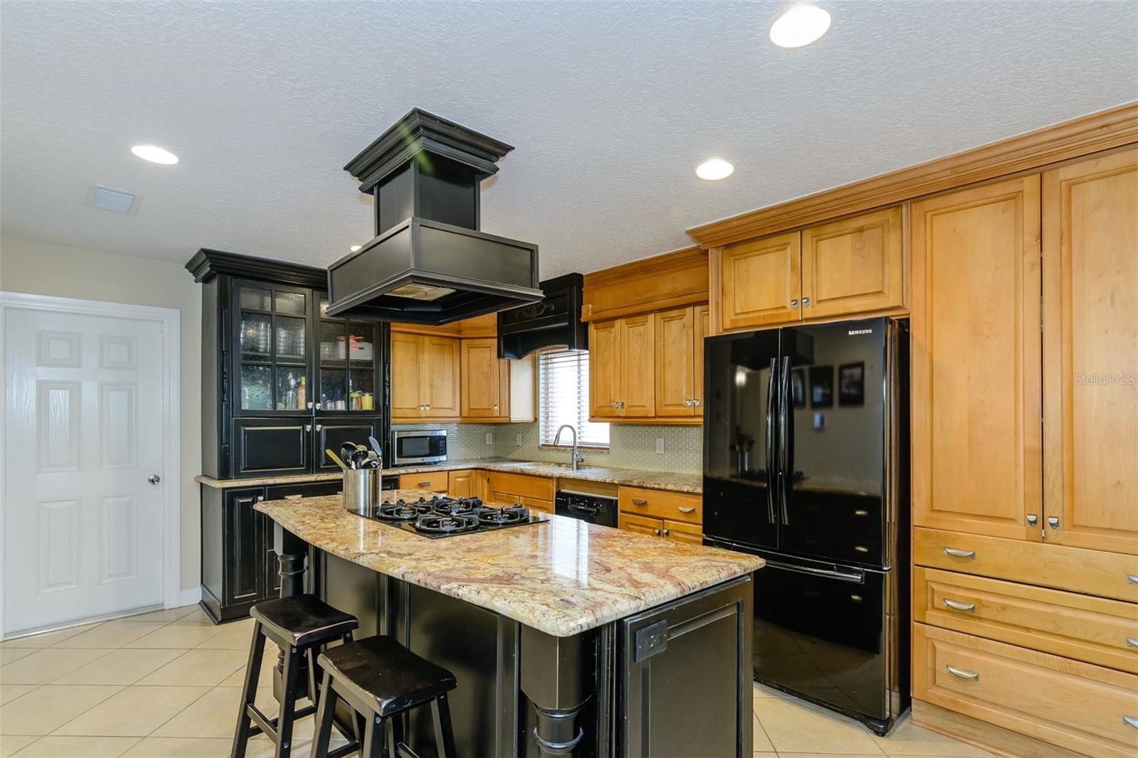The two toned kitchen features stone countertops and wood cabinets with the same tile flooring for a unified, open feel.