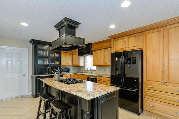 The two toned kitchen features stone countertops and wood cabinets with the same tile flooring for a unified, open feel.