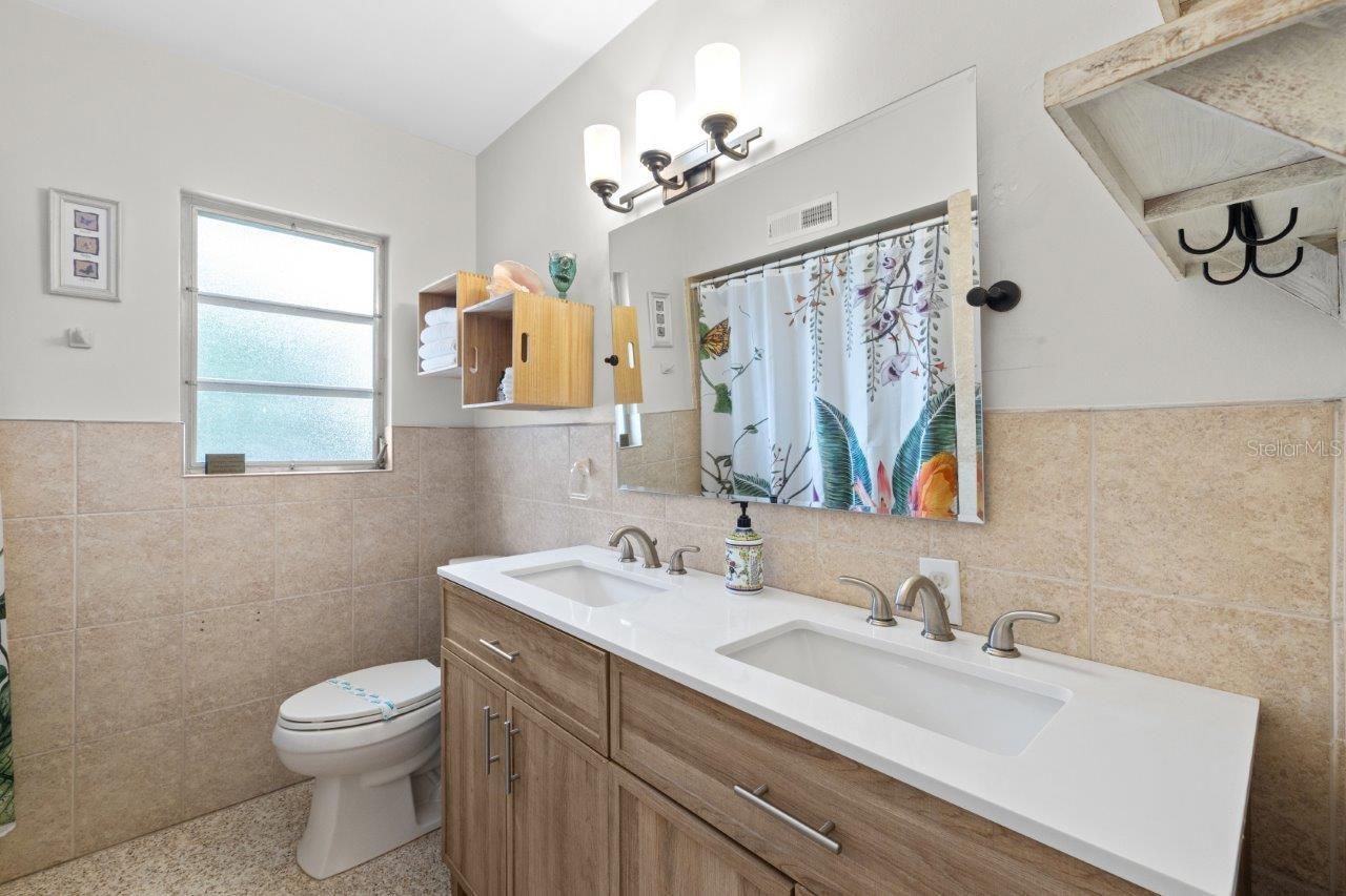 Renovated guest bathroom featuring dual sinks and a walk-in shower.