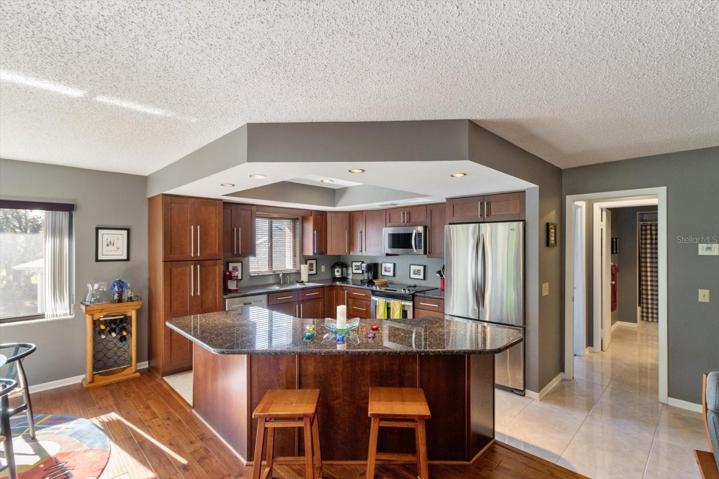 Updated Kitchen w/ Wood Grain Shaker Cabinets w/ European Long Bar Pulls, Granite Countertops, S/S Appliances, Pantry Cabinets, Island w/ Breakfast Bar, Drop Down Tray Ceiling & Porcelain Tile
