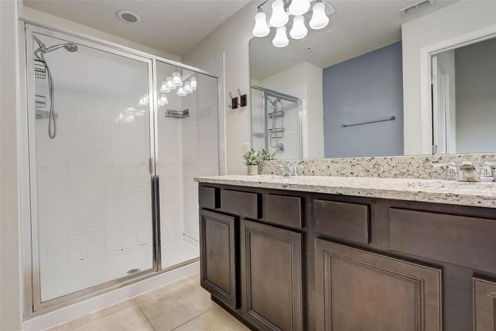 Primary en-suite bath with granite countertop vanity, dual sinks and shower enclosure