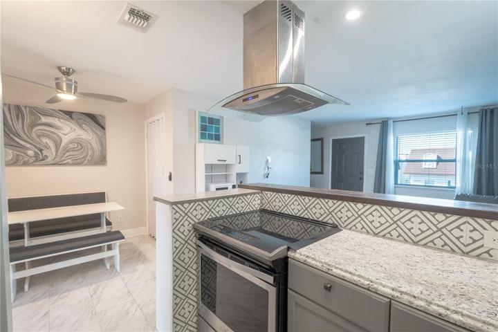 A glass top electric range sits beneath a stainless steel exhaust hood.