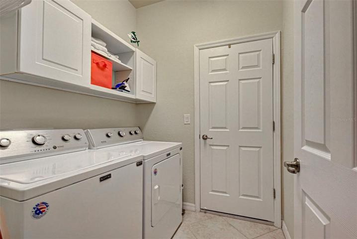 A separate laundry room with shelves and cabinets with a door to the garage.