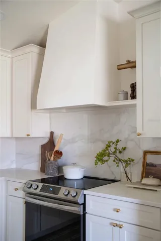 Stunning custom hood, delicately sloped to soften the clean lines of the space, serves as the focal point. Symmetry is achieved with floating shelves and sconces framing the hood on each side.