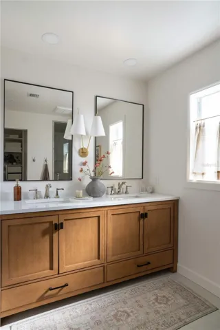 The double vanity in warm wood is accented with polished nickel faucets, designer sconce and large mirrors.