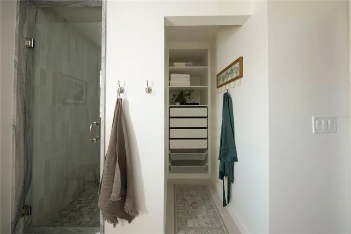 Built-in linen closet with open shelving and pull-out drawers, a separate water closet, porcelain tile floors and recessed LED lighting.