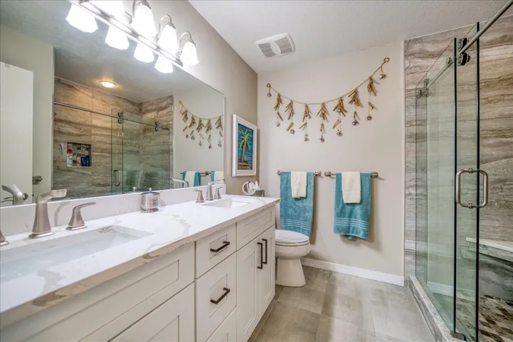 Primary Bathroom with dual sink vanity, large tiled shower with glass door.