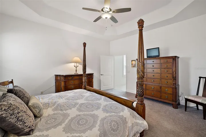 Primary bedroom with tray ceiling and fan.