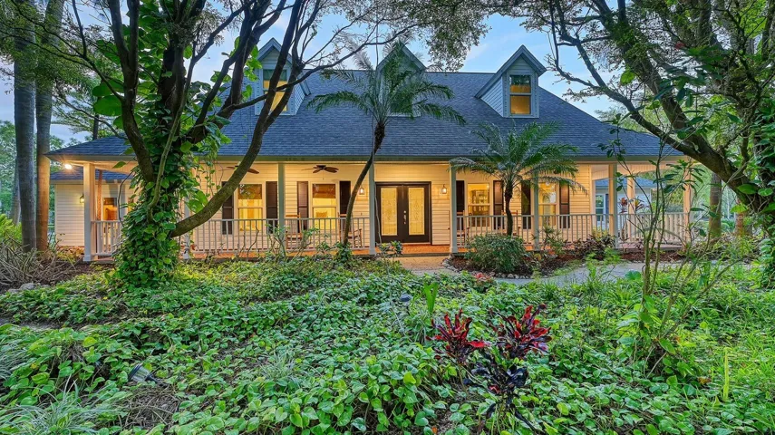 This stunning custom home by Roland Yoder sits on 9+ gorgeous acres, complete with a sweeping front porch overlooking the lush tropical garden.