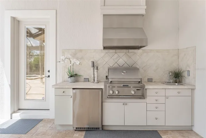 SUMMER KITCHEN is fully equipped w/ REFRIGERATOR, GRILL w/ EXHAUST HOOD, & BUILT IN SINK. Access to POOL BATH via door on L.