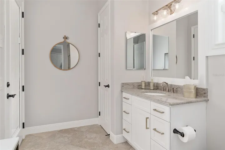 Close up view of POOL BATH access door (L), LINEN CLOSET (center) & sink/vanity w/ GRANITE COUNTERTOP. Note UPDATED gold cabinet hardware, gold faucet, & lighting fixture.