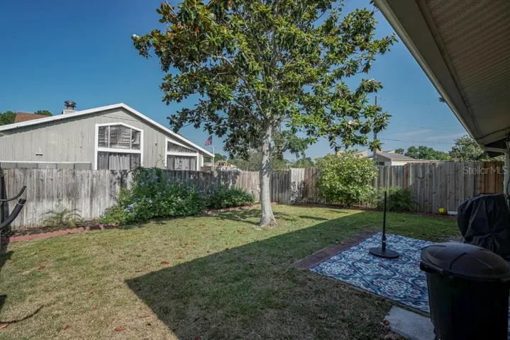Rear fenced yard with Magnolia Tree, Gardenia bushes and paver patio with sliders to Primary Bedroom